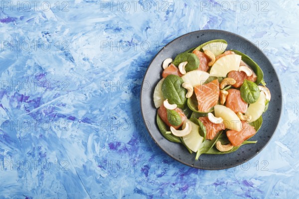 Fresh salmon with pineapple, spinach and cashew on a blue concrete background. Top view, copy