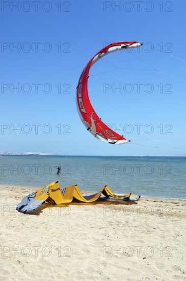 Red sail of kitesurfer kite surfer kite surfer standing close to viewer in the air above beach