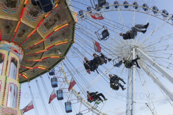 People swinging on a carousel in front of a Ferris wheel in sunny weather at a funfair, Europa Rad,