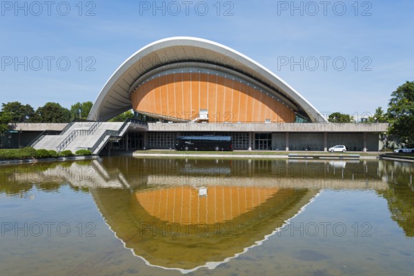 Modern building with curved roof, reflected in the water against a clear sky, House of World