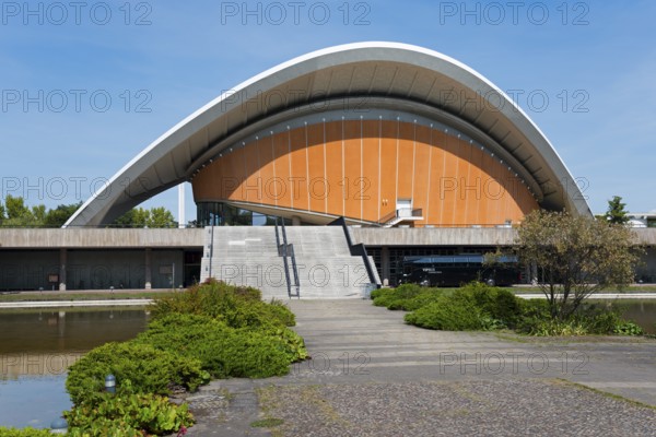 Building with curved roof and wide staircase, surrounded by nature, under a clear sky, House of