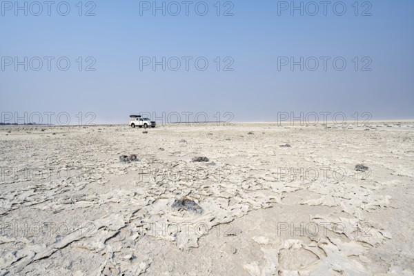 Four-wheel drive Toyota Hilux with roof tent, driving over salt pan, lone car in large wide plain,