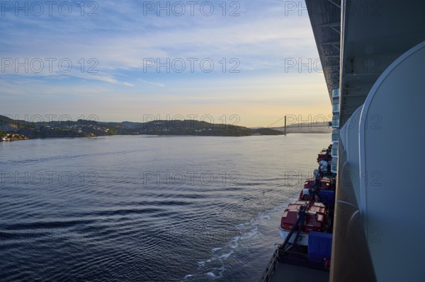 A cruise ship, Mein Schiff 6, on the calm sea, in the background a bridge and hills at sunset,