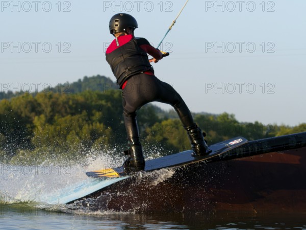 Young man with wakeboard on obstacle, water sports, water skiing in wakepark