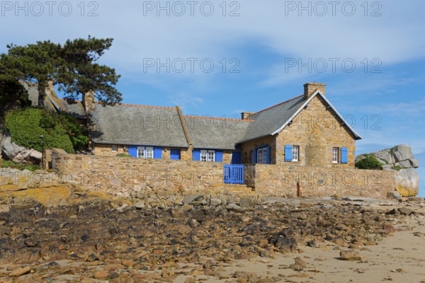 Stone house with blue shutters and a sandy forecourt on a rocky coast, house on the Plage de