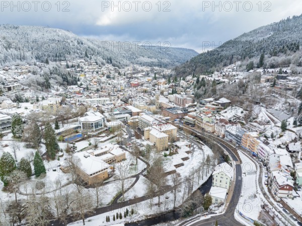 Bird's eye view of a snow-covered town with a river, surrounded by hills and green trees, Bad