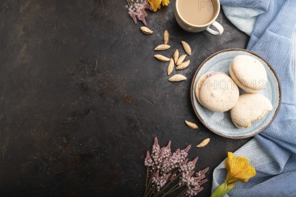 Meringues cakes with cup of coffee on a black concrete background and blue linen textile. Top view,