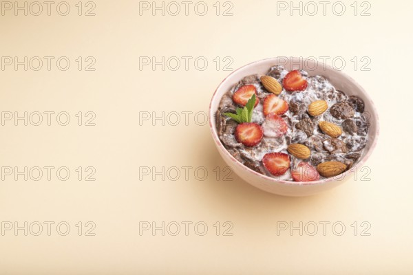 Chocolate cornflakes with milk, strawberry and almonds in ceramic bowl on pastel orange background.