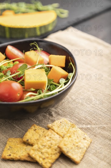 Vegetarian vegetable salad of tomatoes, pumpkin, microgreen pea sprouts on black concrete