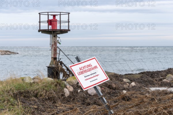Beacon behind a fence with warning sign 'ACHTUNG LEBENSGEFAHR', cloudy sky over the sea, entrance