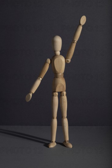 Wooden mannequin stands with raised hand on gray background. protest, attention concept. copy