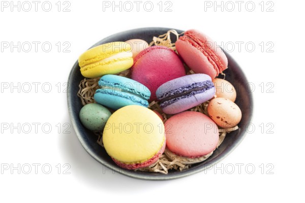 Multicolored macaroons and chocolate eggs in blue ceramic bowl isolated on white background. side
