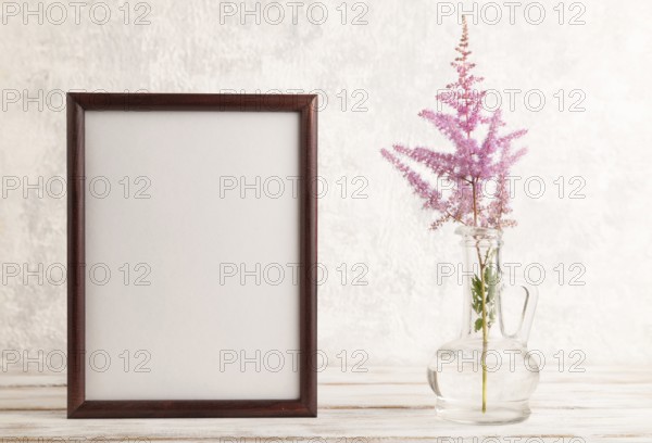 Wooden frame with pink astilbe flowers in glass vase on gray concrete background. side view, copy