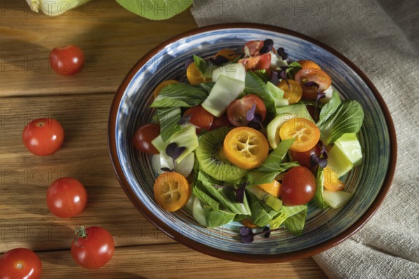 Vegetarian salad of pac choi cabbage, kiwi, tomatoes, kumquat, microgreen sprouts on a wooden