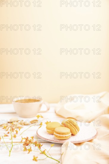 Orange macarons or macaroons cakes with cup of apricot juice on a white wooden background and
