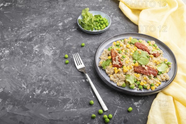 Quinoa porridge with green pea, corn and dried tomatoes on ceramic plate on a gray concrete