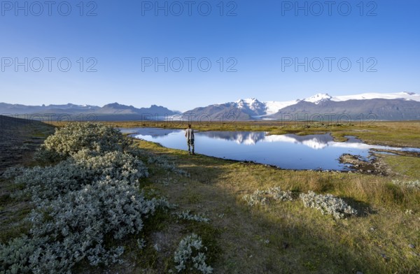 Tourist standing at the lakeshore, reflection in a lake, view of glacier tongues Skaftafellsjökull