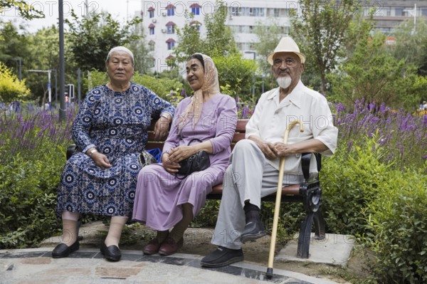 Three elderly Uyghurs sitting on a park bench in the city Hami, Kumul, one of China's ethnic