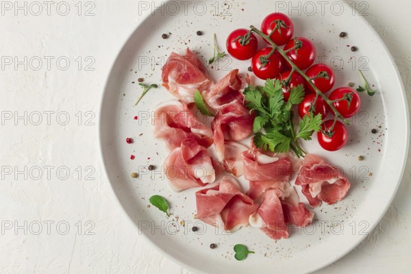 Sliced prosciutto, appetizer, with cherry tomatoes, on a white plate, top view