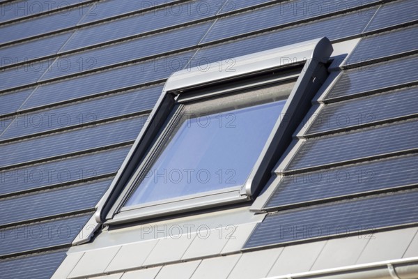 Roof window on a detached house with solar roof tiles. Solar tiles are a beautiful and high-quality