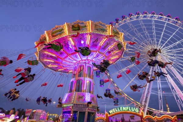 A lively funfair at dusk, illuminated by a large Ferris wheel and a colourful chain carousel,