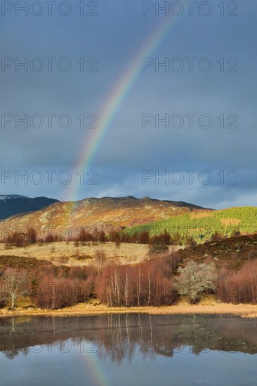 Atmospheric cloudy sky with rainbow over mountainous, partly wooded Highlands in the west of