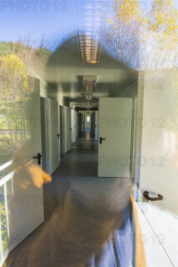 Corridor view with doors and windows, reflection of nature visible in the glass, refugee