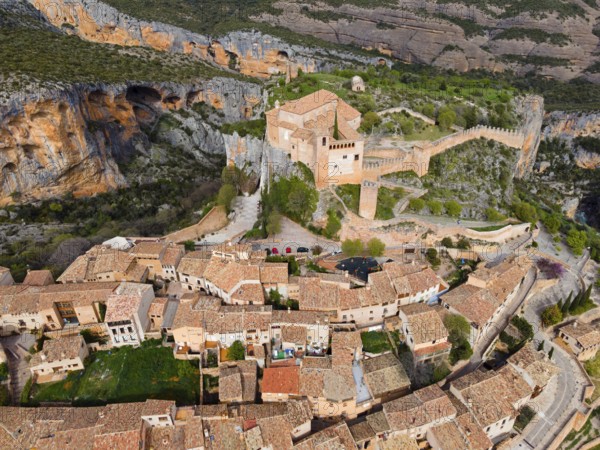 A historic village with tiled roofs and a fortress, nestled in a mountainous landscape, aerial