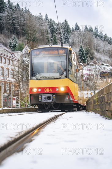 Front view of a tram on snow-covered tracks, surrounded by trees and buildings, Bad Wildbad, Black