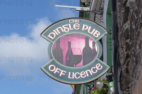 Traditional Dingle pub sign with wine bottles and glass attached to a stone façade under a blue