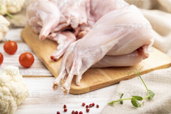 Whole raw rabbit with cauliflower, tomatoes and spices on a white wooden background and linen