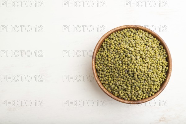 Wooden bowl with raw green mung bean on a white wooden background. Top view, flat lay, copy space