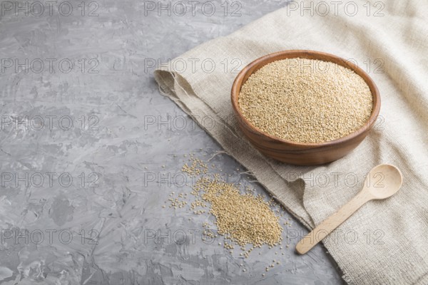 Wooden bowl with raw white quinoa seeds and wooden spoon on a gray concrete background and linen