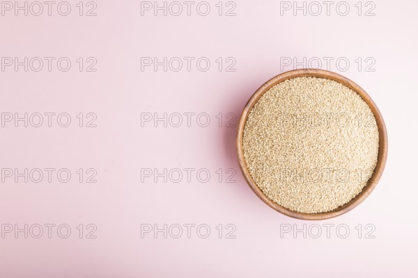 Wooden bowl with raw white quinoa seeds on a pastel pink background. Top view, flat lay, copy space
