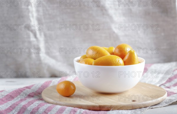 Kumquats in a white plate on a wooden kitchen board, close up