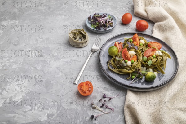 Tagliatelle green spinach pasta with tomato, pea and microgreen sprouts on a gray concrete
