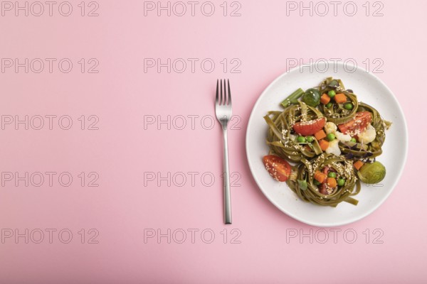 Tagliatelle green spinach pasta with tomato, pea and microgreen sprouts on a pastel pink background