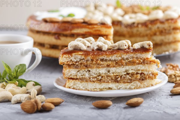 Piece of homemade cake with caramel cream and nuts with cup of coffee on a gray concrete background