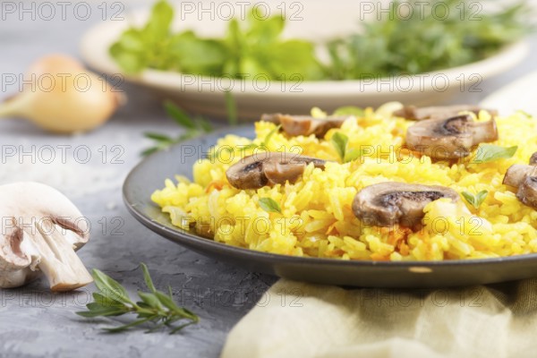 Yellow fried rice with champignons mushrooms, turmeric and oregano on blue ceramic plate on a gray