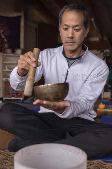 A vertical portrait of a multiracial Latino man with Asian features, holding a Tibetan singing bowl
