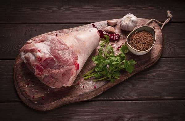 Raw pork knuckle, on a wooden chopping board, with spices, close-up, top view, no people