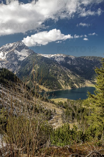 View of the mountain lake Vilsalpsee with surrounding fir trees under a cloudy sky in the