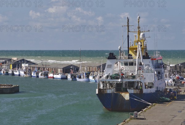 A large fishing boat moored at the harbour, with small fishing boats in the distance and the sea in