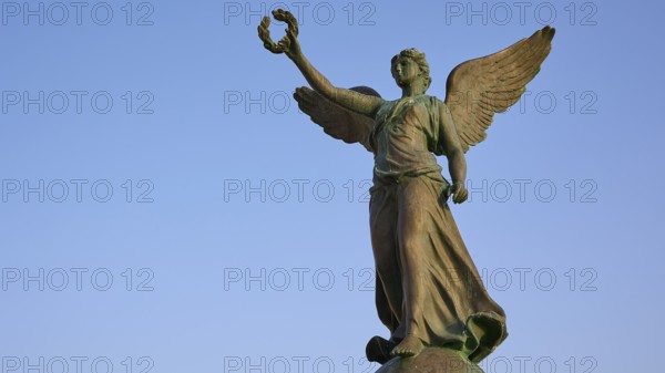 Angel statue with raised hand and outstretched wings towards the sky, harbour area, Rhodes Town,
