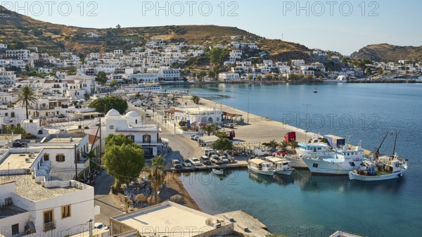 Coastal town with a harbour full of ships, surrounded by hills and blue sea under a sunny sky,