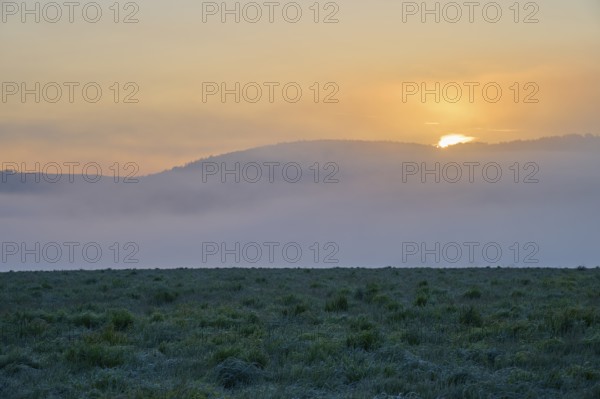 Sunset behind fog-covered hills with a green meadow in the foreground, Mönchberg, Miltenberg,