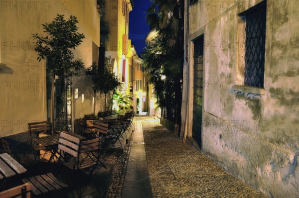 Old Narrow Alley Illuminated at Night with Chairs and Tables in City of Locarno, Ticino,