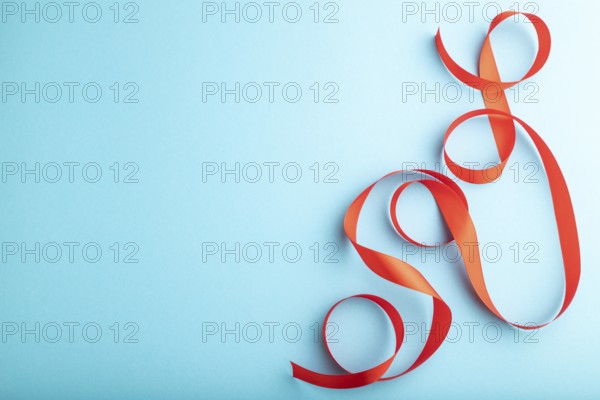 Red coral ribbon on a blue pastel background. Celebration concept. Top view, copy space, flat lay
