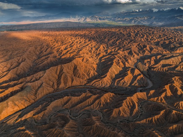River bed runs through a landscape of eroded hills, badlands at sunset, mountain peaks of the Tian