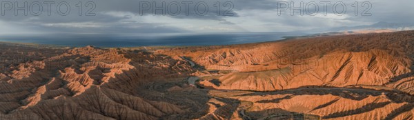 Riverbed runs through a landscape of eroded hills, badlands at sunset, Issyk Kul Lake in the